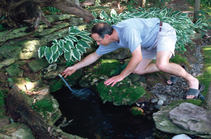 author bending over to show a small stream of water flowing into the moss and rocks