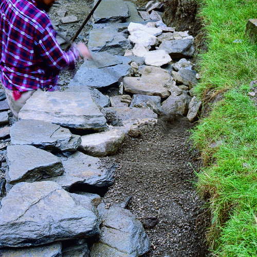 person working on retaining wall; adding dirt behind the stones