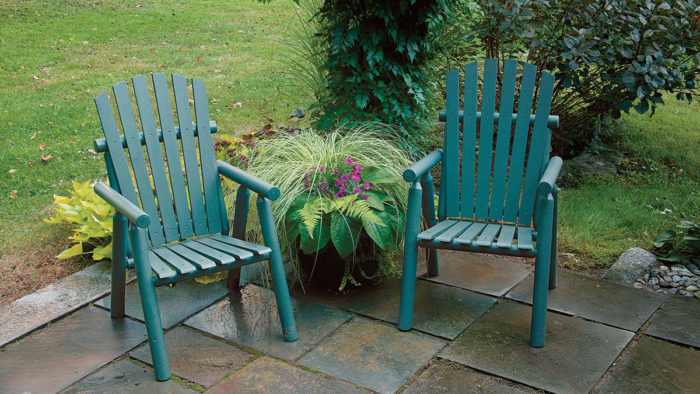 Two chairs painted green, on a small patio with a plant next to them