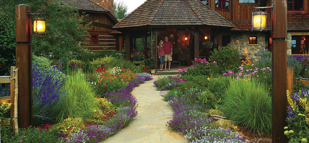 Author and her husband in front of their house, with a pathway surrounded on both sides by colorful flowers, including sweet alyssum