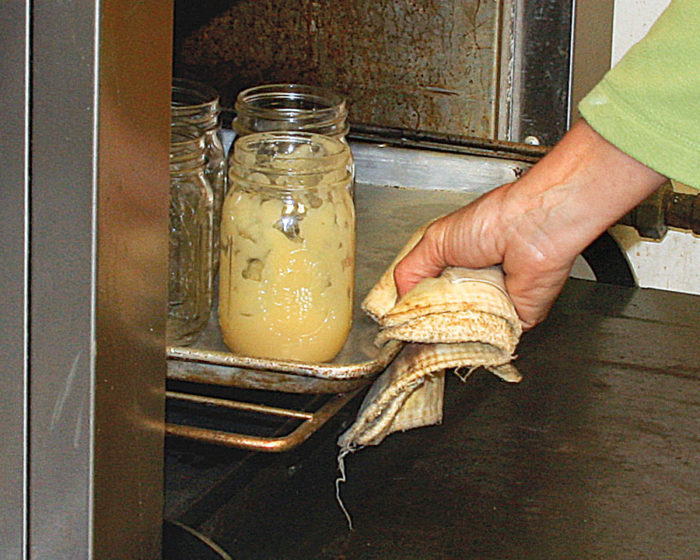 Hand taking out mason jars on a tray with a potholder from the oven