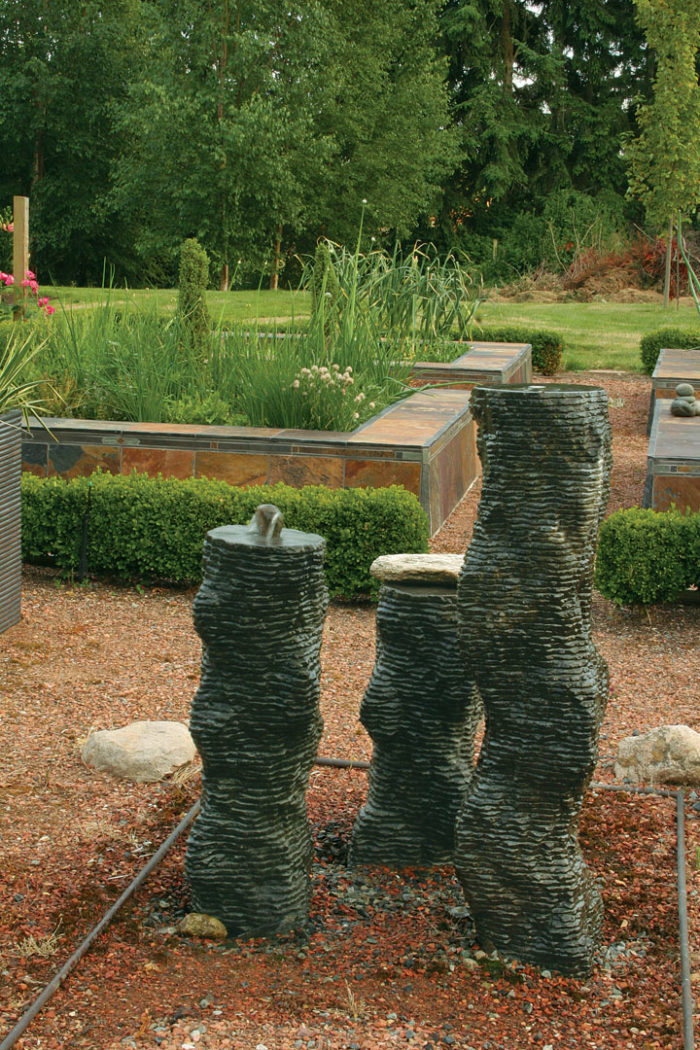 unique column fountains spit water alongside raised vege­table beds