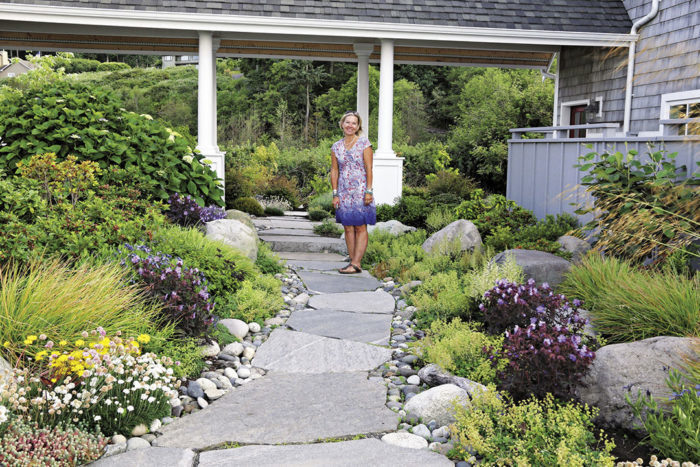 a woman standing on a stone path with low growing plants and hardscaping on both sides