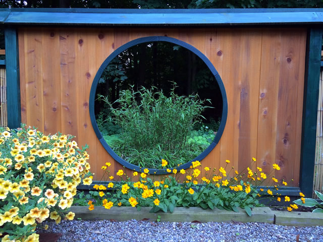 Colorful yellow flowers in front of a moon window in a fence