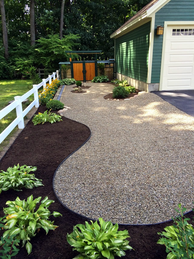 another view toward the garage and gate showing plants, mulch and rock path