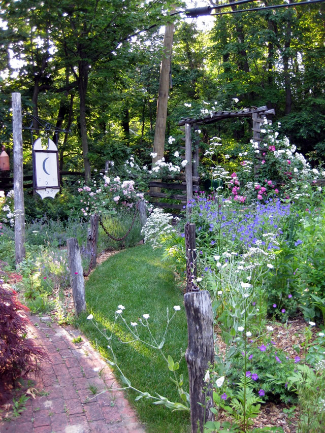 sign, brick path leading up to the pergola, various flowers