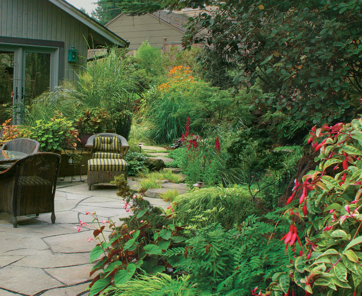 This patio makes use of potted plants to soften a short stack of angular stairs, while a border with plenty of curves makes room for big plants that provide screening.