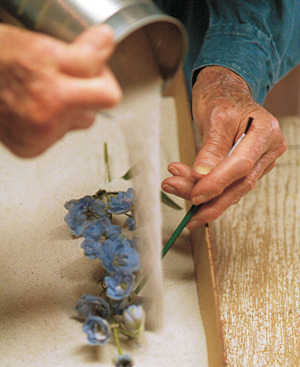 Woman using a paintbrush to carefully support the flower while pouring the sand