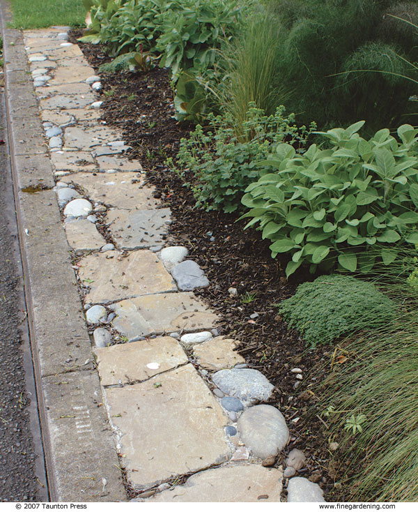 Pebbles fill the spaces between large flat stones in this edging along a streetside curb.