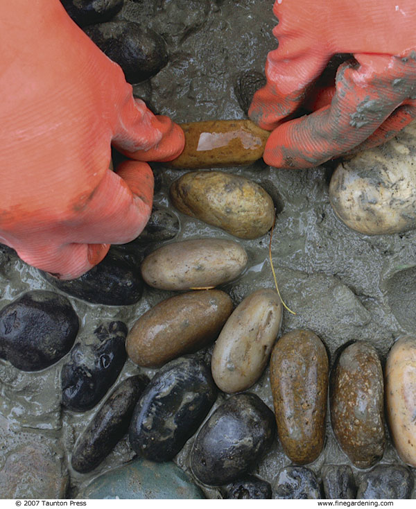 Close-up of author pressing small stones into mortar, wearing gloves.