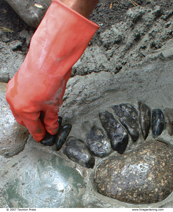 Close-up of author pressing small stones closely together into mortar, wearing gloves.