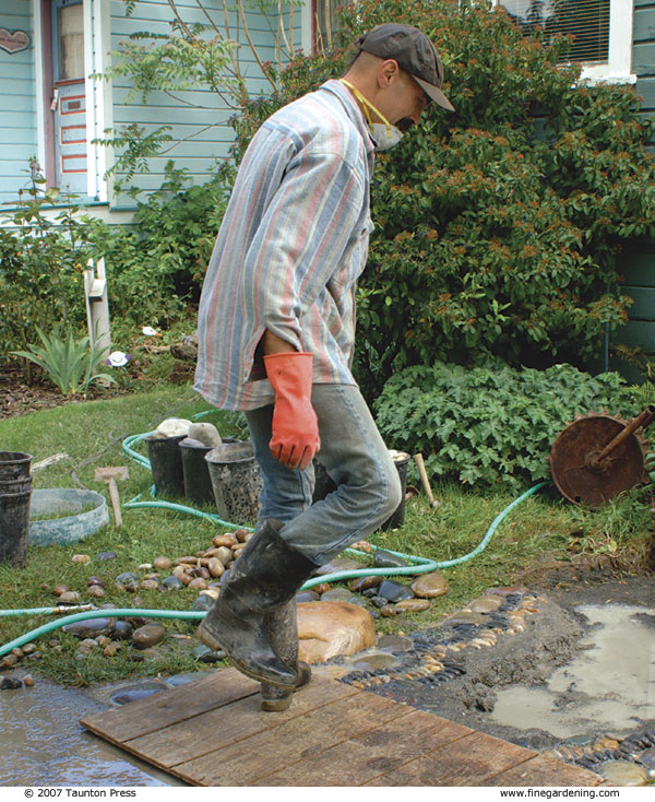 Author stepping on board to press stones into mortar on walkway.