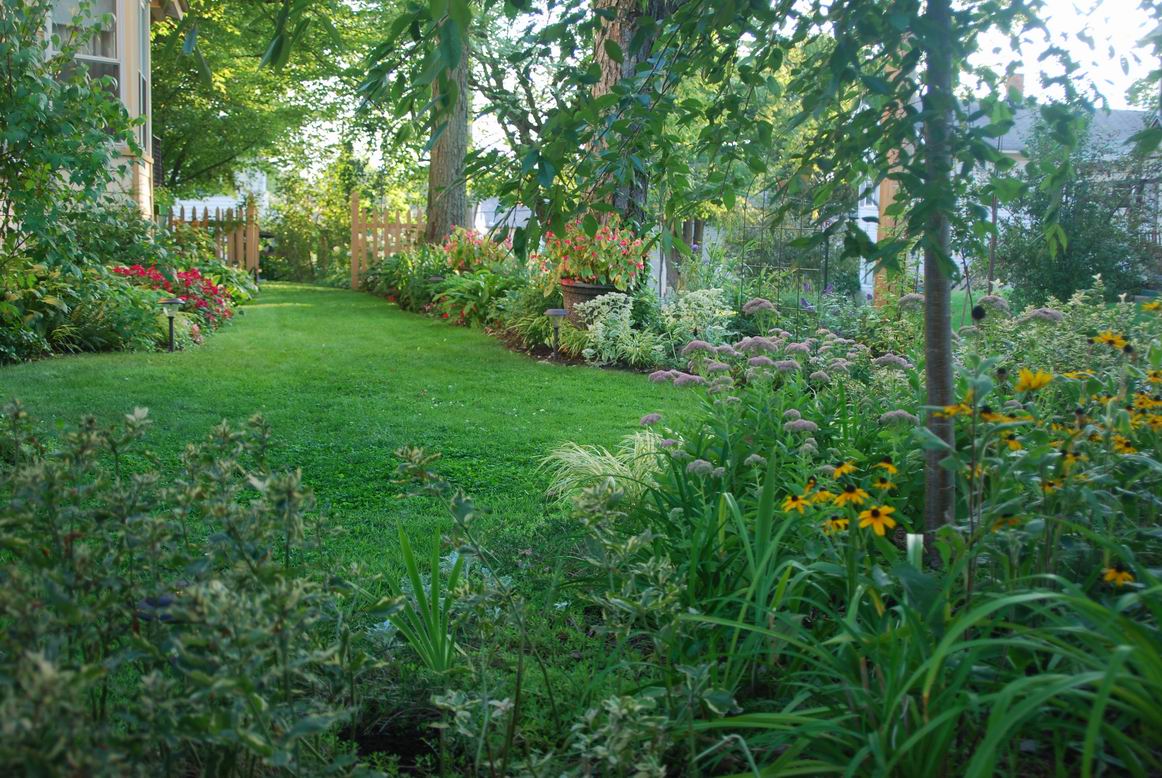 lush green lawn with flowers on either side; open fence in the distance