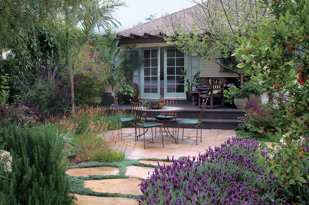 garden around a path and patio with open space around furniture; table and chairs and then the house in the background