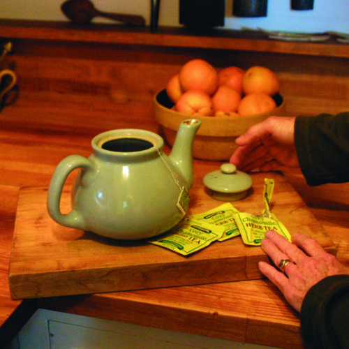 chamomile tea steeping in a pot next to bowl of oranges on a counter