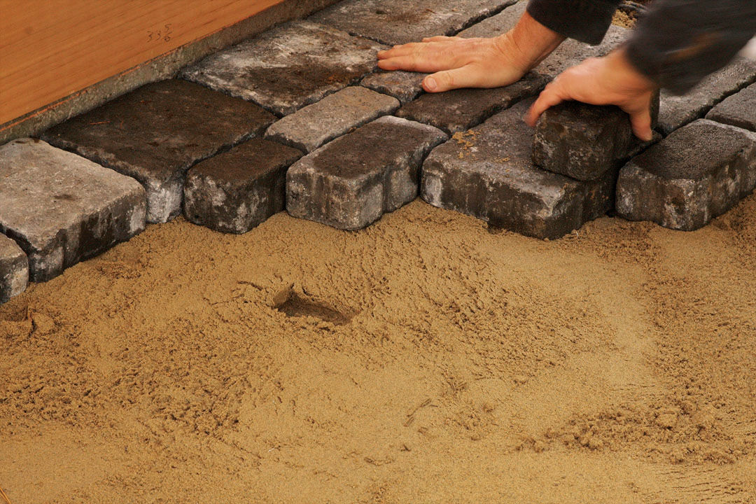 hands laying the first row of pavers along the line