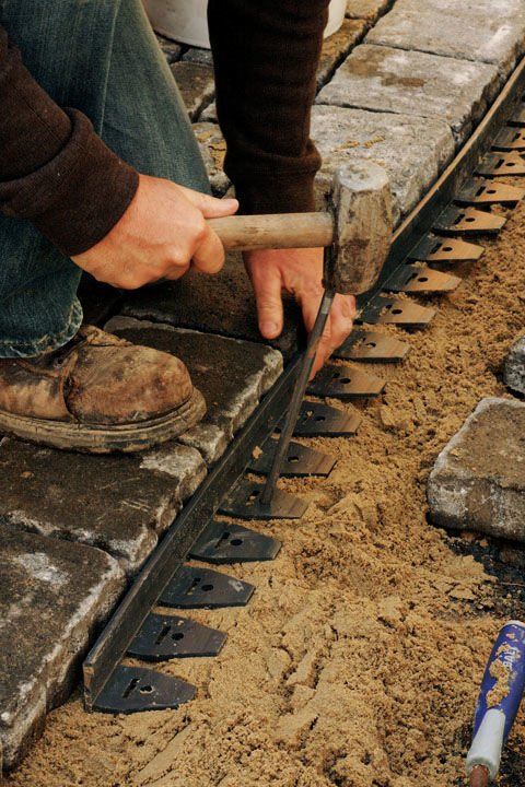 man securing the edging with metal spikes, keeping it a few inches below the pavers so that it won’t be seen.