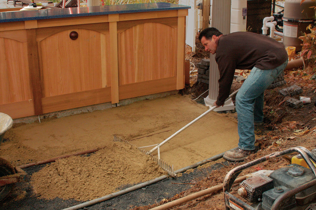 man spreading sand evenly with a metal rake