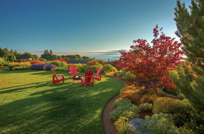 green lawn, colorful plants and red Adirondack chairs overlooking a vista with blue sky