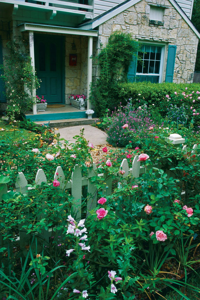 Stone cottage entryway with a white picket fence and many colorful flowers