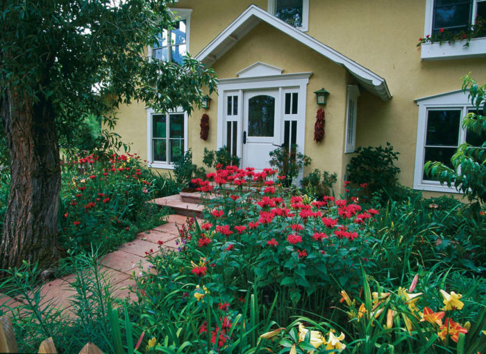 Yellow house with a brick path and many colorful flowers