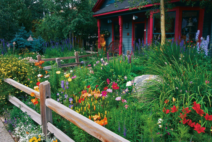 blue house with red accents with small colorful garden and split rail fence