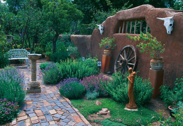 colored walkway with cow skulls on a wall, a wagon wheel and other art, statuary and plants