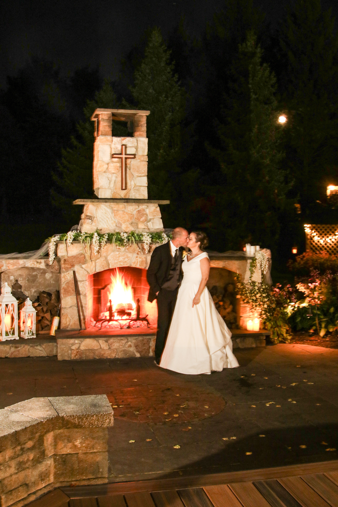 A newly married couple kisses in front of an outdoor fireplace