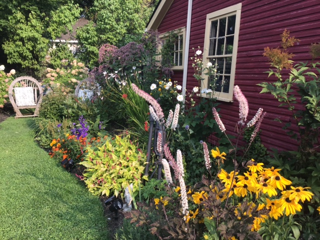 Diverse flowers blooming next to a red barn