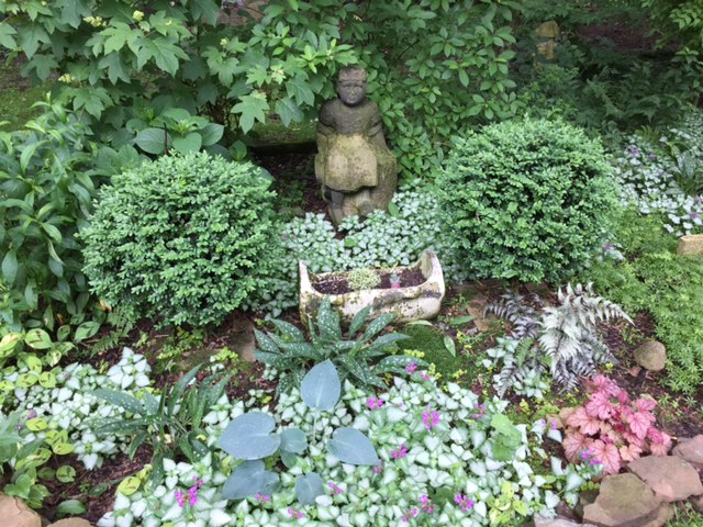 A small stone statue of a man behind a shaded garden