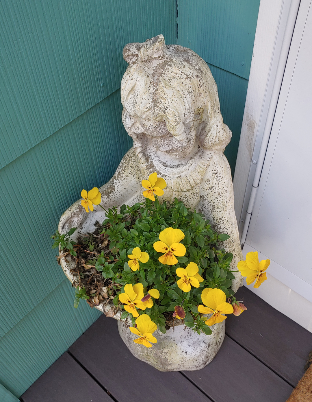 Planter in the shape of a girl holding a basket with yellow flowers growing in it