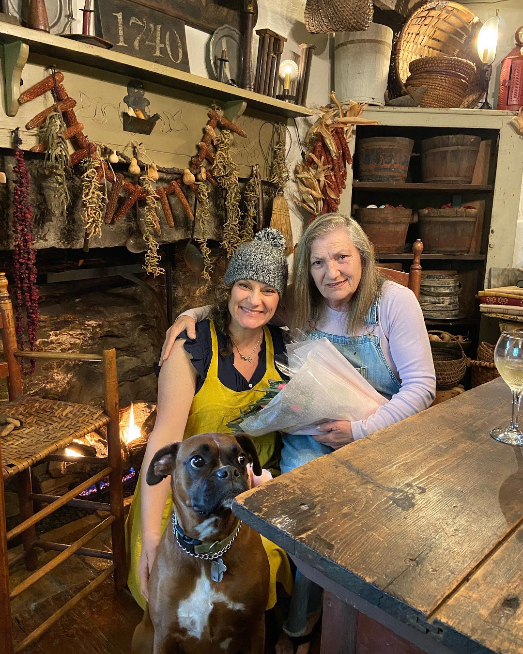 Two women sitting in a room filled with antique tools and a large fireplace