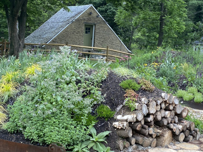 A garden planted on a mound with logs at one end. A small building is visible behind.