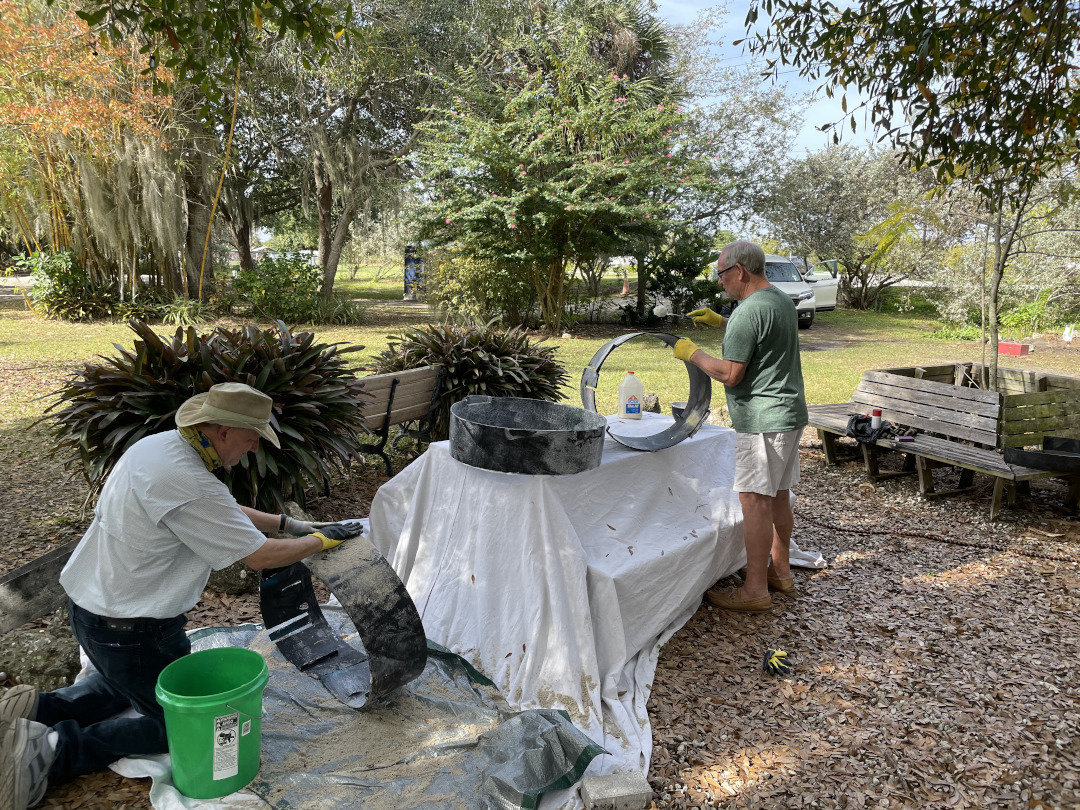 Two men painting black plastic rings with glue and covering them with sand