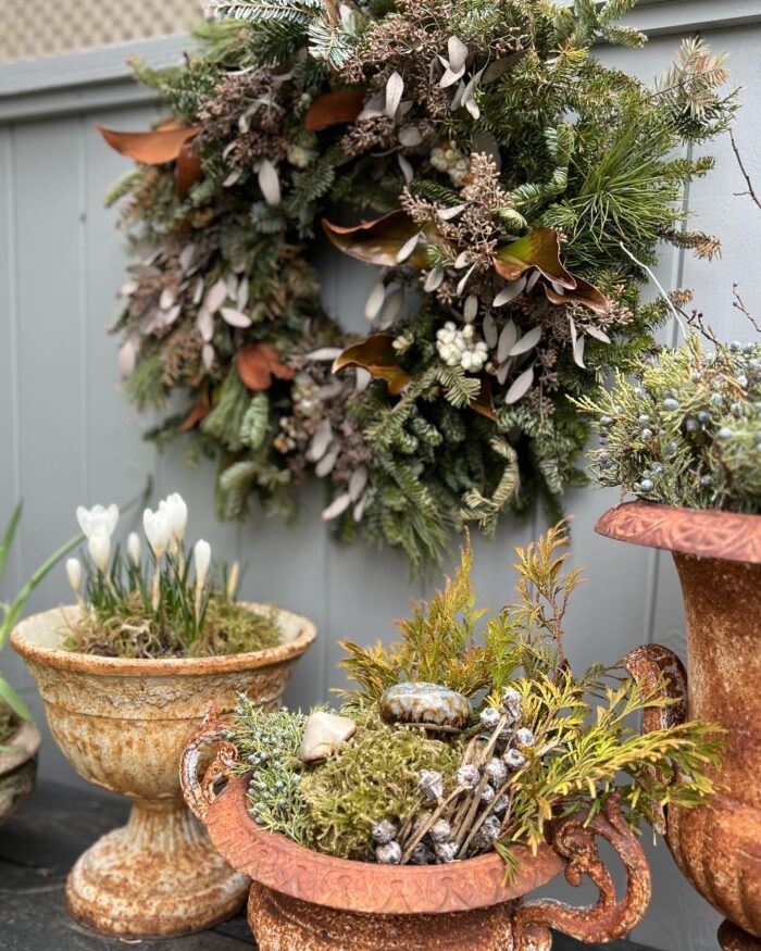 winter wreath behind winter container arrangements in rusty urns