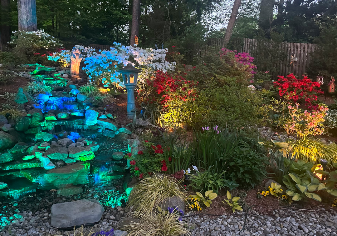 Jardín de ladera y cascada al atardecer con coloridas luces de jardín