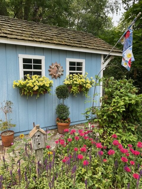 close up of garden shed with window boxes and many flowers planted in front