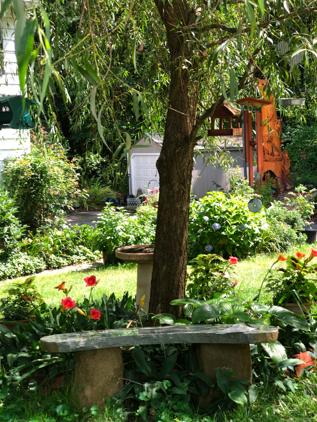 stone garden bench under a tree and in front of red flowers