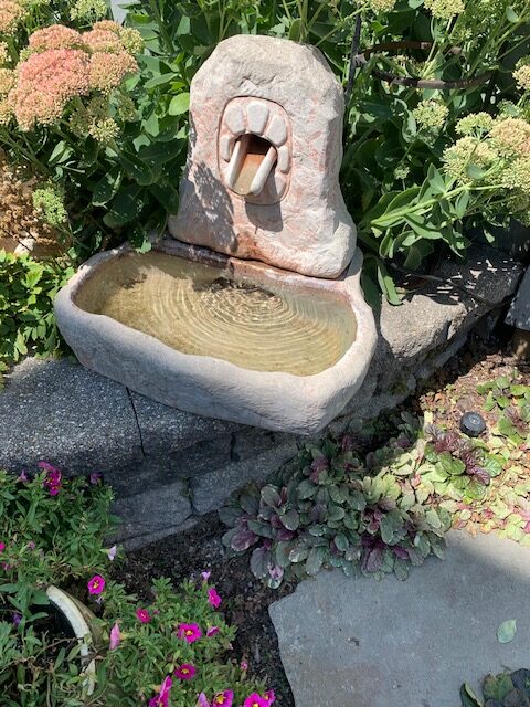 small stone water fountain on edge of garden bed