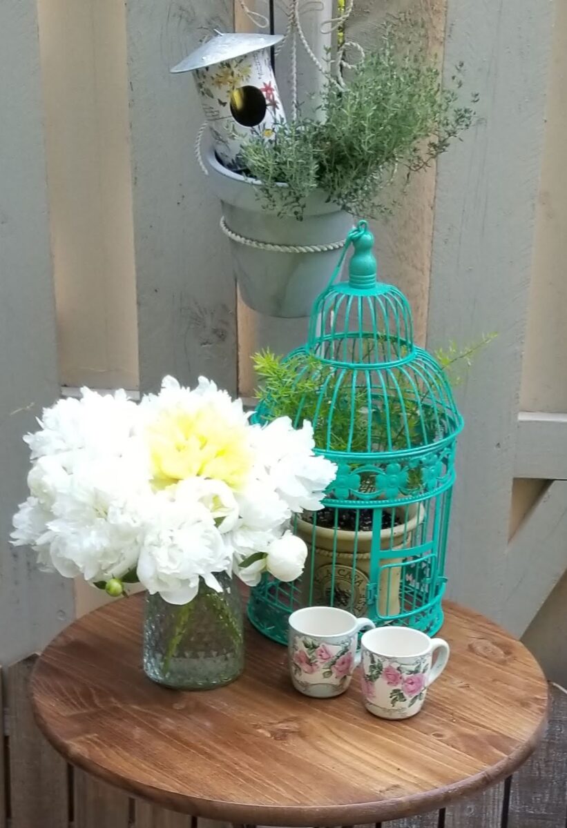 small table with vase full of white peonies and containers planted with herbs