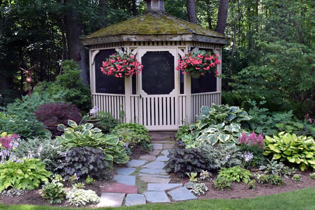 gazebo in the shade surrounded by various foliage plants and pink flowers