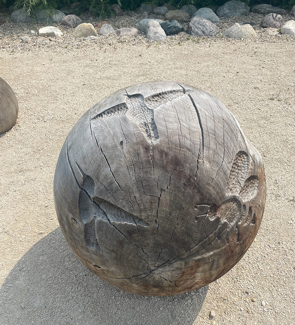 a bee and hummingbird carved into large wooden ball
