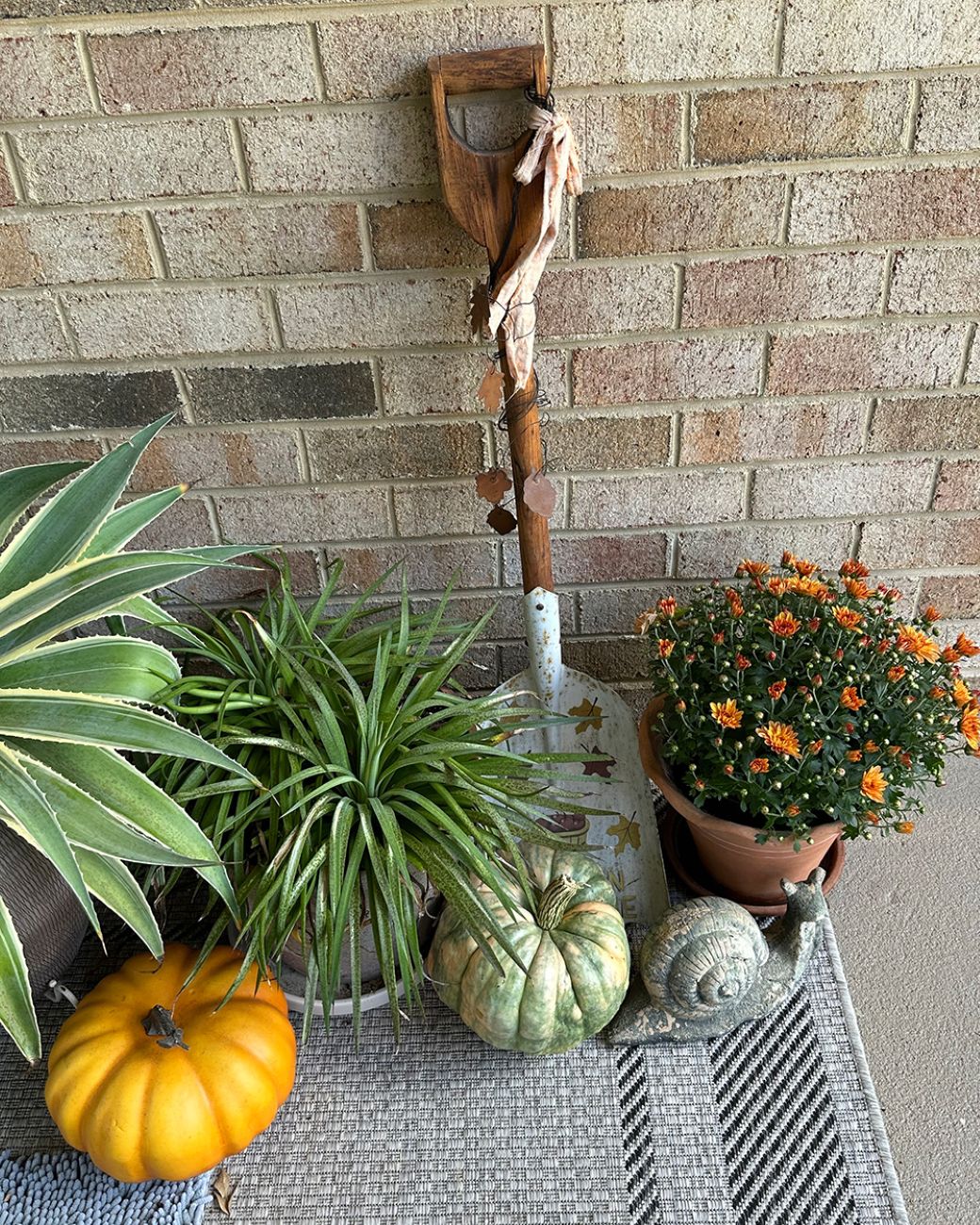 Fall porch display with orange mum, pumpkins, sculptural foliage, and garden decor