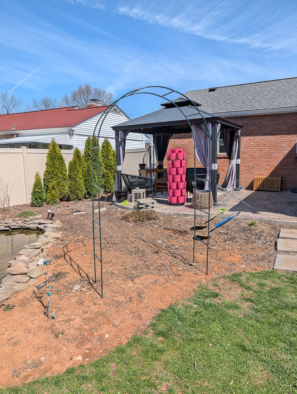 Bare spring garden with new metal arch beside enlarged pond and patio