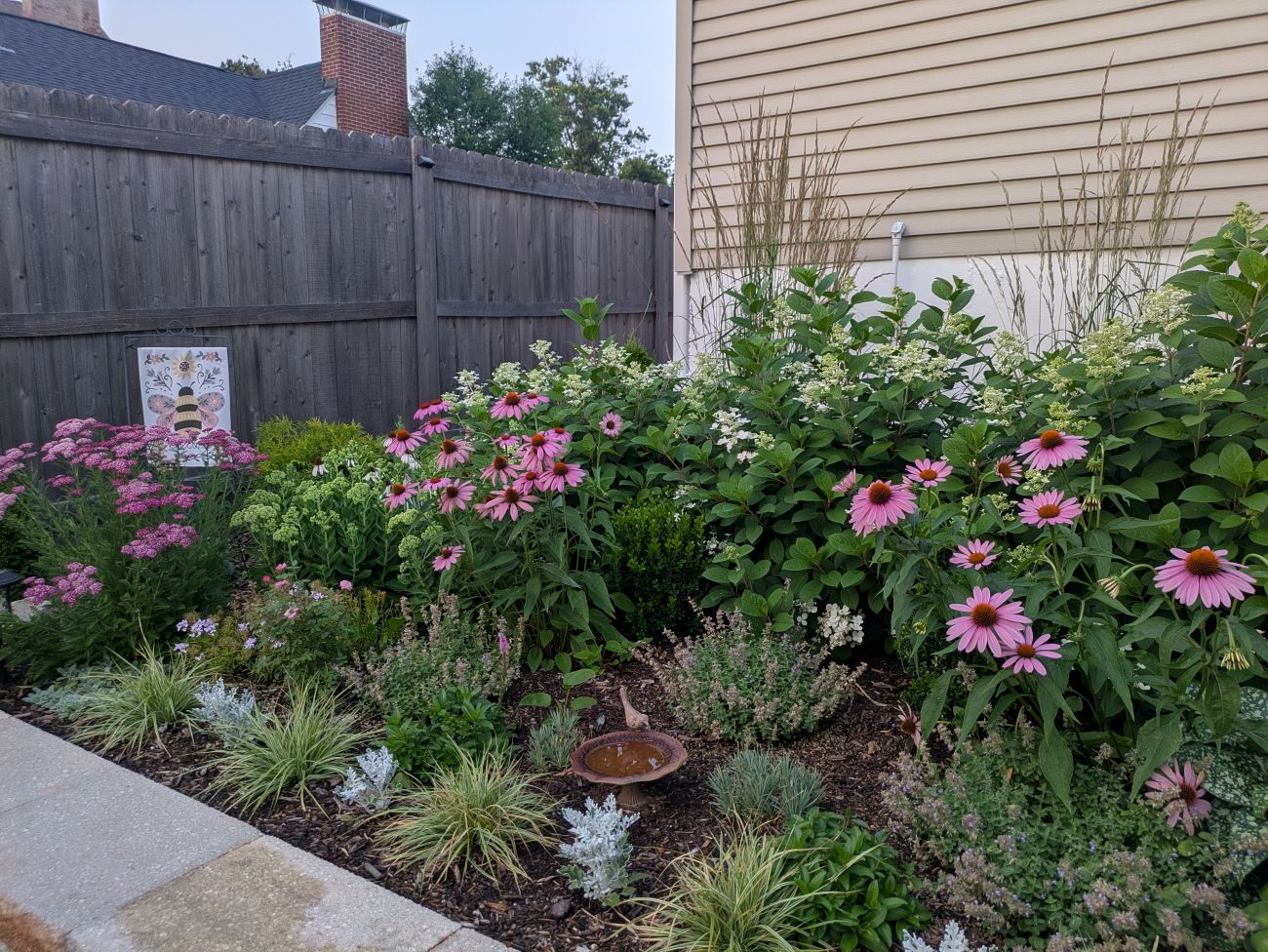 Dense perennial bed filled with pink coneflowers, white hydrangeas, purple catmint, yarrow, sedges, and other flowering plants.