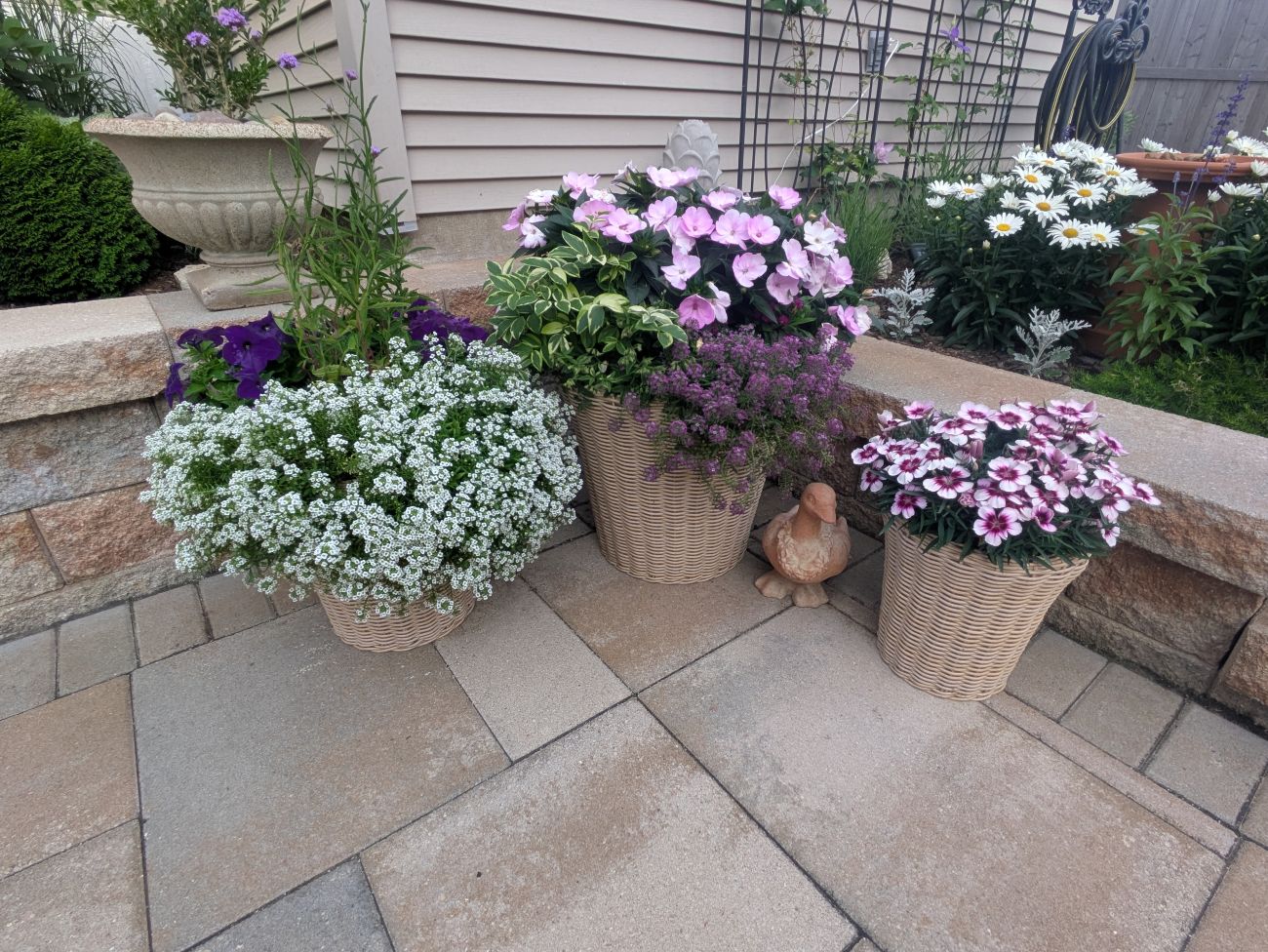 Three basket planters filled with pink, purple, and white flowers beside a stone patio.