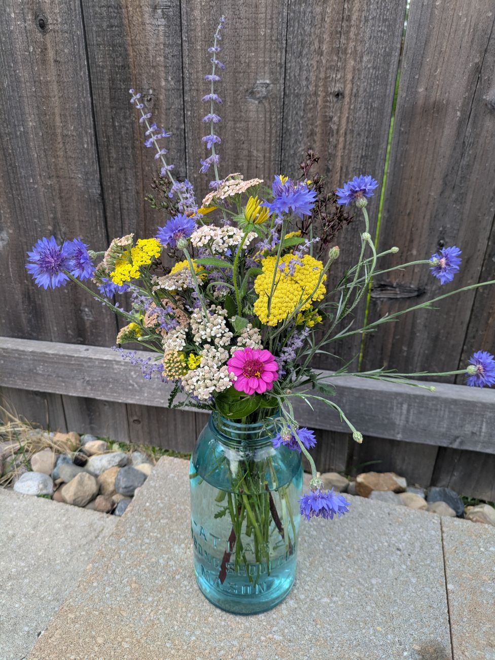 Blue, yellow, pink, and white cut flowers arranged in a vintage blue glass Atlas jar.