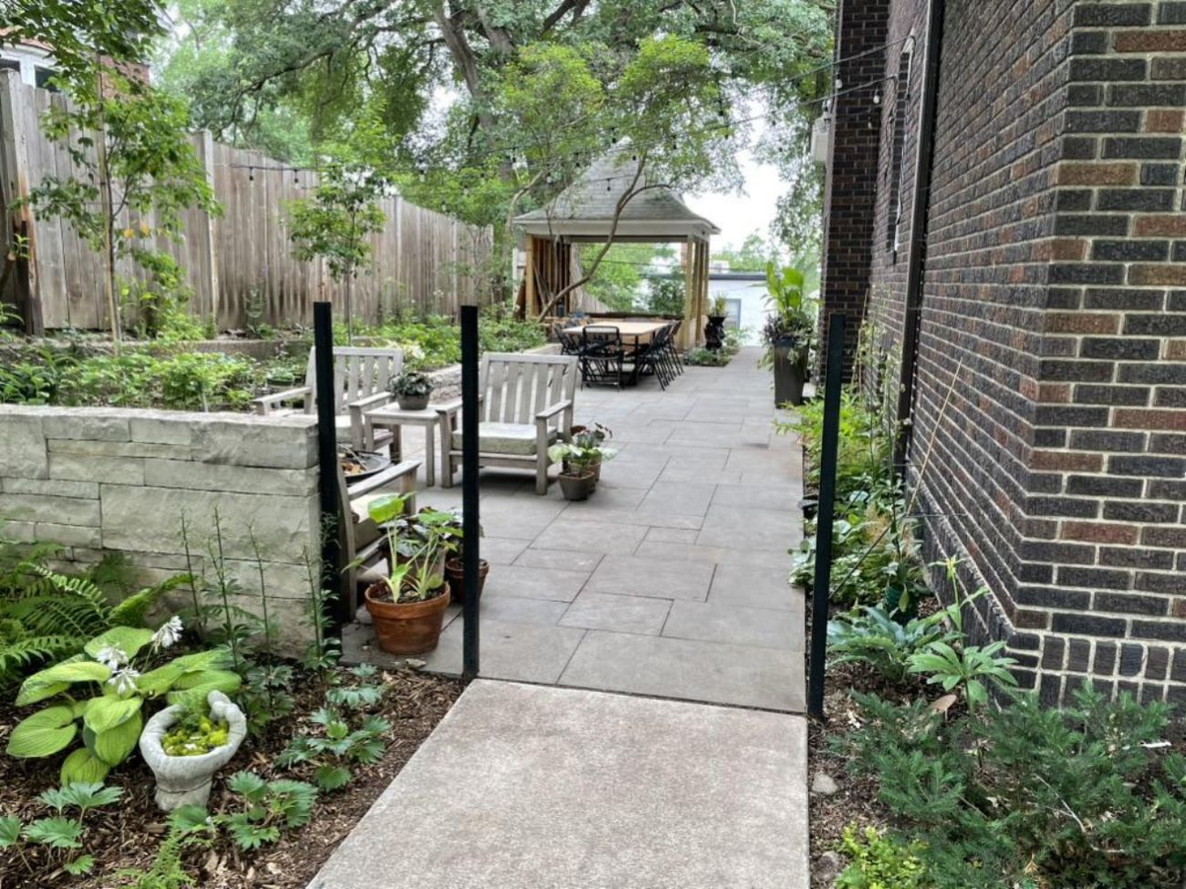 Expanded bluestone patio with stone retaining walls, outdoor seating, garden beds, and a gazebo at the far end.