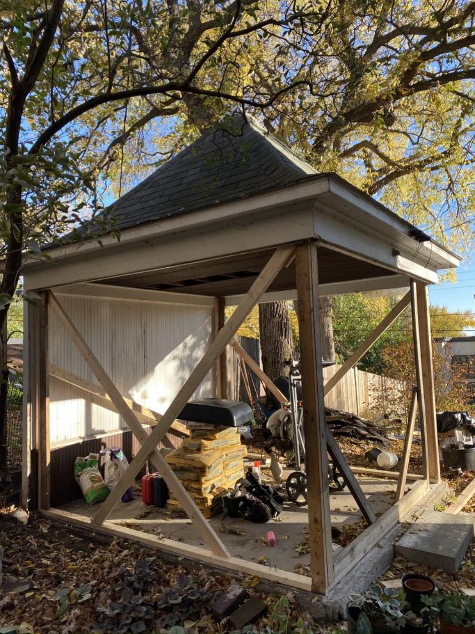 Gazebo stripped down to its roof, concrete foundation, framing, and temporary braces during reconstruction.