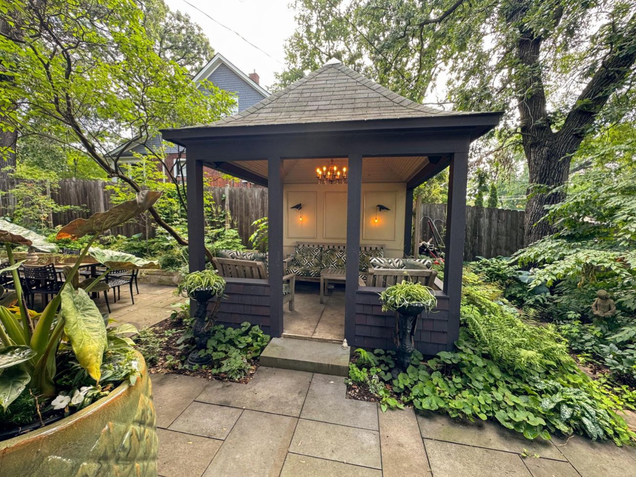Dark-painted screened gazebo surrounded by layered shade plantings at the end of a bluestone patio.